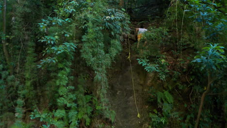 Male-person-climbing-the-rock-with-rope-in-dense-forest,-aerial