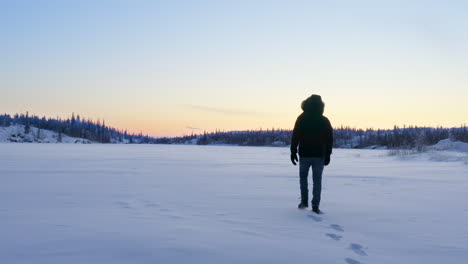 Aerial-of-person-walking-on-snowy-frozen-lake-in-wilderness,-canada