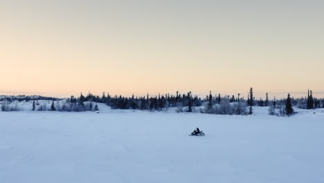 Aerial-follow-of-person-driving-snowmobile-on-frozen-lake-in-evening