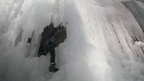 Kletterer-Verwendet-Eispickel,-Um-Auf-Einen-Felsvorsprung-Zu-Klettern,-Der-Sich-An-Einer-Großen-Eiswand-Befindet
