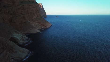 Aerial-view-of-young-man-running-towards-cliff-edge-during-sunrise-on-mountain-surrounded-by-silent-and-calm-sea-in-Benidorm-city-in-Spain