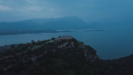 Aerial-view-of-Rocca-di-Manerba-summit-cross-in-front-of-Lake-Garda-at-Twilight