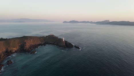 Drone-aerial-footage-of-a-lighthouse-at-dawn-and-splashing-ocean-waves-hitting-the-rocks