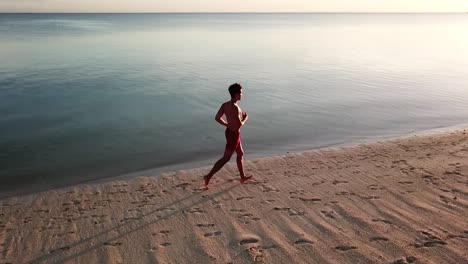 Aerial-tracking-shot-of-a-man-jogging-on-a-beautiful-tropical-beach