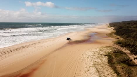 Aerial-view-of-a-blue-4x4-vehicle-driving-on-an-island-next-to-the-sea-in-Australia