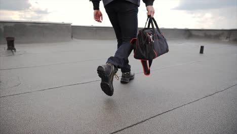 Young-man-engineer-with-bag-on-rooftop-of-the-building-walking-in-boots-in-slow-motion