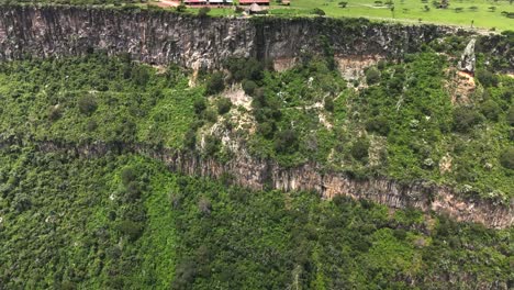 Small-red-rooftop-buildings-on-cliff-edge-lush-mountain-Mexico-Huasca-landscape-aerial-rising-push-in