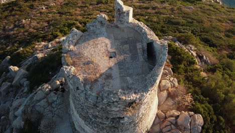 Overhead-circular-view-of-Torre-di-Porto-Giunco-tower-surrounded-by-rocks-and-shrubs-in-Sardinia-in-Italy-with-people-around