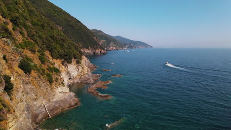 Drohnenblick-Auf-Ein-Schiff,-Das-Im-Stillen-Und-Ruhigen-Meer-Des-Dorfes-Portovenere-In-Italien-Segelt-Und-Tagsüber-Felsen-Und-Grün-Auf-Einer-Klippe-Mit-Blick-Auf-Das-Wasser-Hat