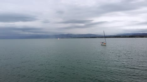 Passing-slowly-by-a-sailboat-on-dark-calm-waters-of-Lake-Constance,-Switzerland