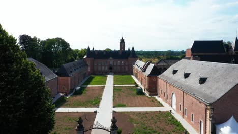 Aerial-view-of-entrance-and-garden-of-Alden-Biesen-Castle-in-Belgium,-Germany-spread-across-large-area-with-greenery-and-landscape-during-day