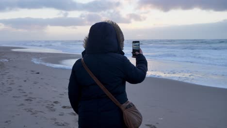 Weite-Aufnahme-Einer-Jungen-Frau,-Die-An-Einem-Windigen-Tag-Am-Schönen-Strand-Von-Sylt-Ein-Video-Mit-Einem-Smartphone-Macht