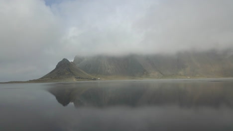 Brumosa-Cordillera-Vestrahorn-Reflejada-En-Aguas-Poco-Profundas-De-Playa-Volcánica-Negra,-Stokksnes,-Sur-De-Islandia---Toma-Aérea-De-Drones