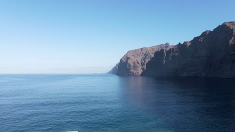 Aerial-drone-view-ascending-over-Los-Gigantes-harbor-towards-steep-cliffs-by-the-sea-in-Tenerife,-Canary-Islands