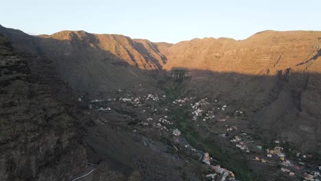 Aerial-drone-footage-of-village-in-the-middle-of-steep-rugged-mountains-during-sunrise-in-Gran-Rey-valley,-La-Gomera,-Canary-Islands