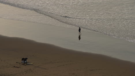 Person-Walking-At-The-Shoreline-Of-Beach-With-Calm-Waves-During-Sunset