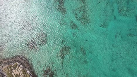 Birds-eye-view-of-turquoise-blue-water-bay-with-rocks-visible-under-the-pristine-waters-during-a-peaceful-day