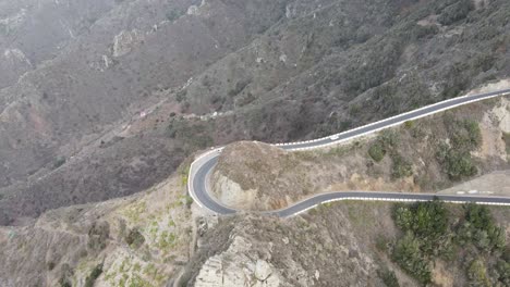 Aerial-view-of-white-car-driving-in-a-winding-road-at-a-rocky-mountain-in-Tenerife,-Canary-islands