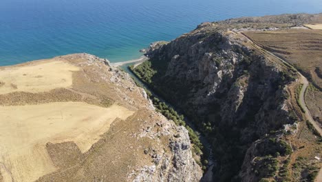 Aerial-view-of-river-surrounded-by-a-palm-forest-in-Preveli-gorge,-flowing-to-the-Mediterranean-sea-in-Crete,-Greece
