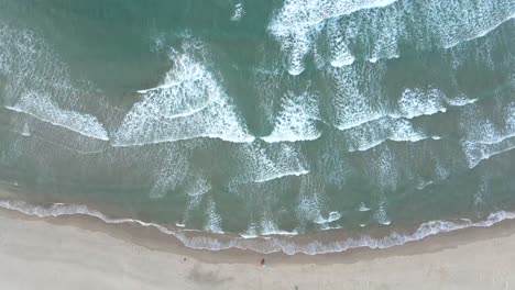 Aerial-drone-shot-of-big-surfing-waves-and-surfers-paddling-in-the-Cantabrian-coast,-Meron-beach