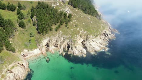 Aerial-drone-flight-above-beautiful-rock-cliff-mountain-hill-with-pine-trees-by-the-ocean