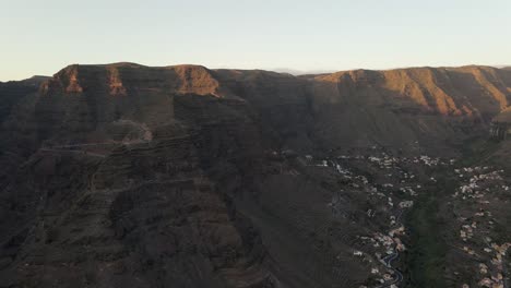 Drone-footage-of-steep-mountains-and-village-in-Gran-Rey-valley,-La-Gomera,-the-Canary-Islands-with-warm-sunset-light