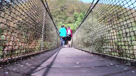 Adventurous-couple,-man-and-woman,-crossing-a-suspension-bridge-in-Fragas-do-Eume,-Galicia,-during-a-sunny-day
