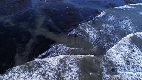 Drone-tilt-down-and-fly-over-tide-pools-at-Mavericks-Beach,-California-during-sunset
