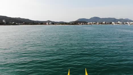 Aerial-flyover-kayaker-team-paddling-over-the-ocean-with-Florianopolis-Island-in-backdrop,Brazil