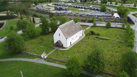 Die-Alte-Kirche-Von-Kinsarvik-Norwegen---Eine-Der-ältesten-Kirchen-Norwegens,-Erbaut-Im-Jahr-1160---Drehbare-Luftaufnahme-Der-Kirche-Und-Des-Friedhofs