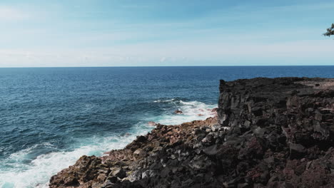 Blue-waves-of-Pacific-Ocean-break-against-basalt-cliff,-Hawaii
