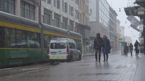 Straßenbahn,-Polizeiauto-Und-Menschen-Mit-Masken-Auf-Der-Zentralen-Straße-Einer-Großstadt-An-Einem-Kalten-Und-Verschneiten-Wintertag-Während-Einer-Covid-pandemie