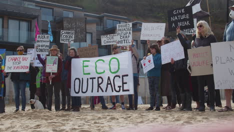 Protesting-all-gather-on-the-beach-in-front-of-the-Carbis-Bay-Hotel-in-St-Ives,-Cornwal-holding-various-anti-hotel-placards