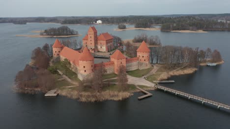 AERIAL:-Flying-Away-from-Trakai-Island-Castle-with-Forest-and-Lake-Surrounding-Majestic-Historical-Fortress