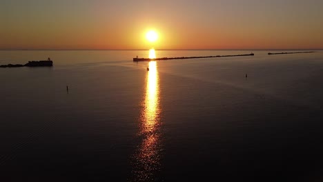 Beautiful-aerial-vibrant-high-contrast-sunset-over-calm-Baltic-sea,-rock-pier-at-Port-of-Liepaja-,-distant-sailing-boat,-wide-angle-drone-shot-moving-forward
