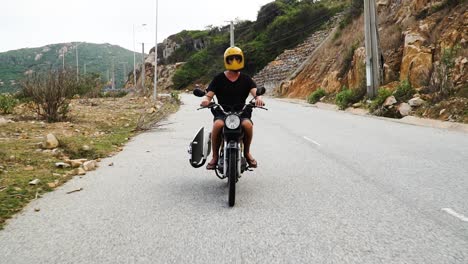 Man-with-surfboard-travels-on-motorbike,-Vietnam-Ninh-Thuan-province-road-trip