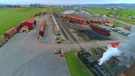 An-Aerial-View-of-an-Antique-Restored-Steam-Train-and-Passenger-Coaches-Approaching-With-Smoke-and-Steam-Pulling-into-the-Yard-and-Station-as-a-Second-Steam-Train-is-Leaving-as-Seen-by-a-Drone