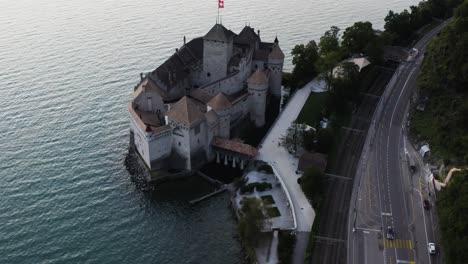 Aerial-shows-Chillon-castle-from-above-and-tilting-up-to-Lausanne-city,-Switzerland