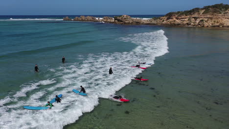 Aerial:-Young-surf-class-students-attempt-to-stand-on-a-small-wave