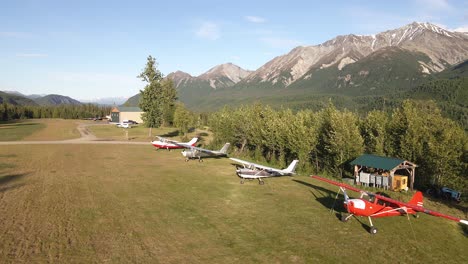 Imágenes-Aéreas-Rodadas-A-Lo-Largo-De-Aviones-Estacionados-A-Lo-Largo-De-Una-Pista-De-Aterrizaje-De-Hierba-En-La-Cordillera-Talkeetna-De-Alaska
