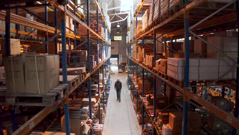 Bald-man-walking-through-a-warehouse-aisle-with-racks-and-packed-boxes