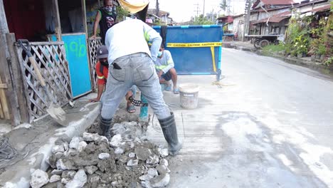 Foremen-wearing-safety-reflective-vests-use-their-shovel-and-demolition-hammer-to-perform-deep-excavation-beside-the-road-and-gutter-for-installing-new-water-piping-from-the-main-water-line