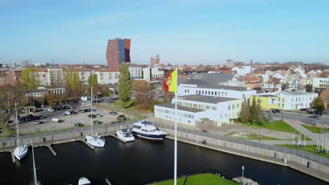 A-flag-with-the-coat-of-arms-of-the-city-of-Klaipeda-is-filmed-on-the-mast,-a-view-of-the-city-with-a-harbor-for-boats-is-visible