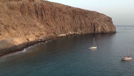 Rocky-high-cliff-coastline-of-Tenerife-island-with-couple-sailboats,-aerial-view