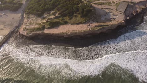 Beautiful-Aerial-top-down-view-of-the-cliffs-and-crashing-waves-of-Mar-del-Plata-on-a-sunset-evening-at-Acantilados,-Argentina