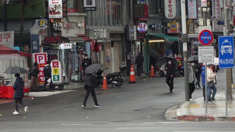 Dongdaemoon-Design-Plaza-in-old-Seoul,-South-Korea-on-a-rainy-day-with-traffic-and-people-walking-by-with-umbrellas-and-wearing-face-masks