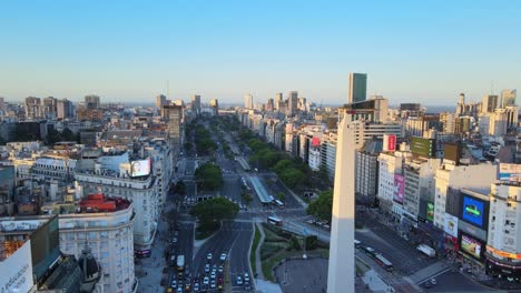Establishing-drone-flying-along-9-de-julio-avenue-capturing-metropolitan-cityscape-with-commercial-advertising-billboards-and-iconic-Obelisco,-the-national-historic-monument-of-Buenos-Aires