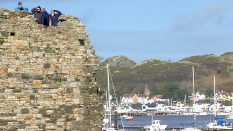 Tourists-overlooking-town-harbour-boats-from-medieval-waterfront-stone-wall