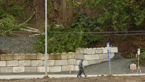 People-Walking-and-Car-Drives-Past-Concrete-Wall-Built-to-Protect-from-Landslide-and-Hillside-House-at-Risk-of-Collapse,-tilt-up-reveal