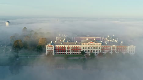 Aerial-reveal-shot-of-majestic-Jelgava-Palace-castle-building-between-dense-foggy-day-in-Latvia